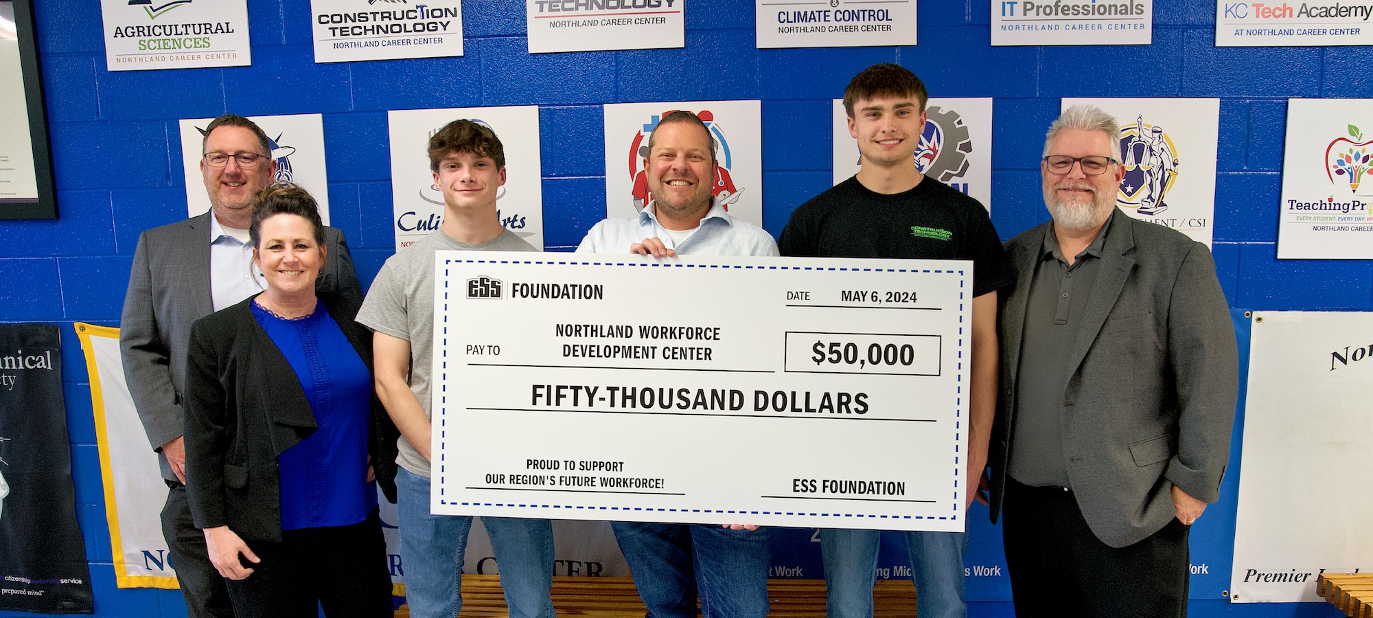 A group of six people pose with a life-size $50,000 check from the ESS Foundation to Northland Workforce Development Center.